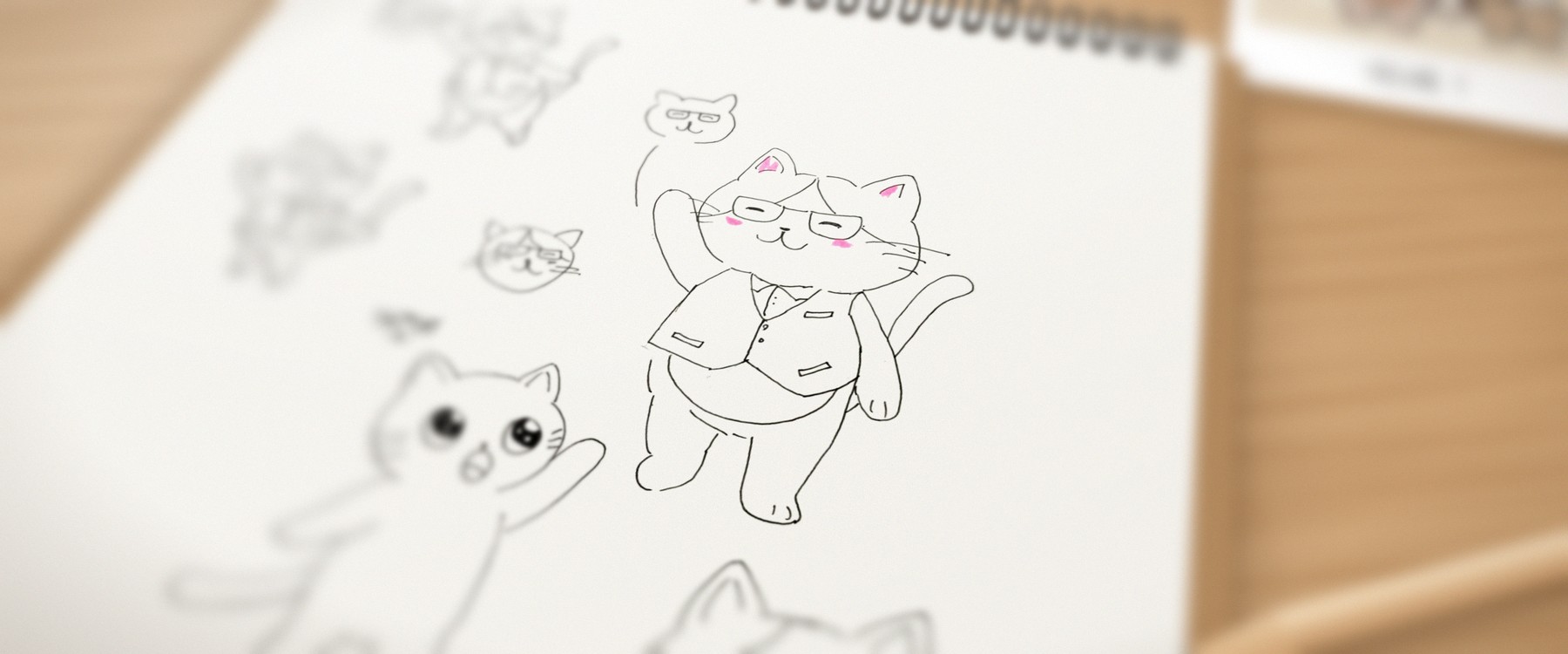 スパイラルノートに描かれた、眼鏡とベストのねこのラフ。ピントはねこに合い、まわりはぼけている